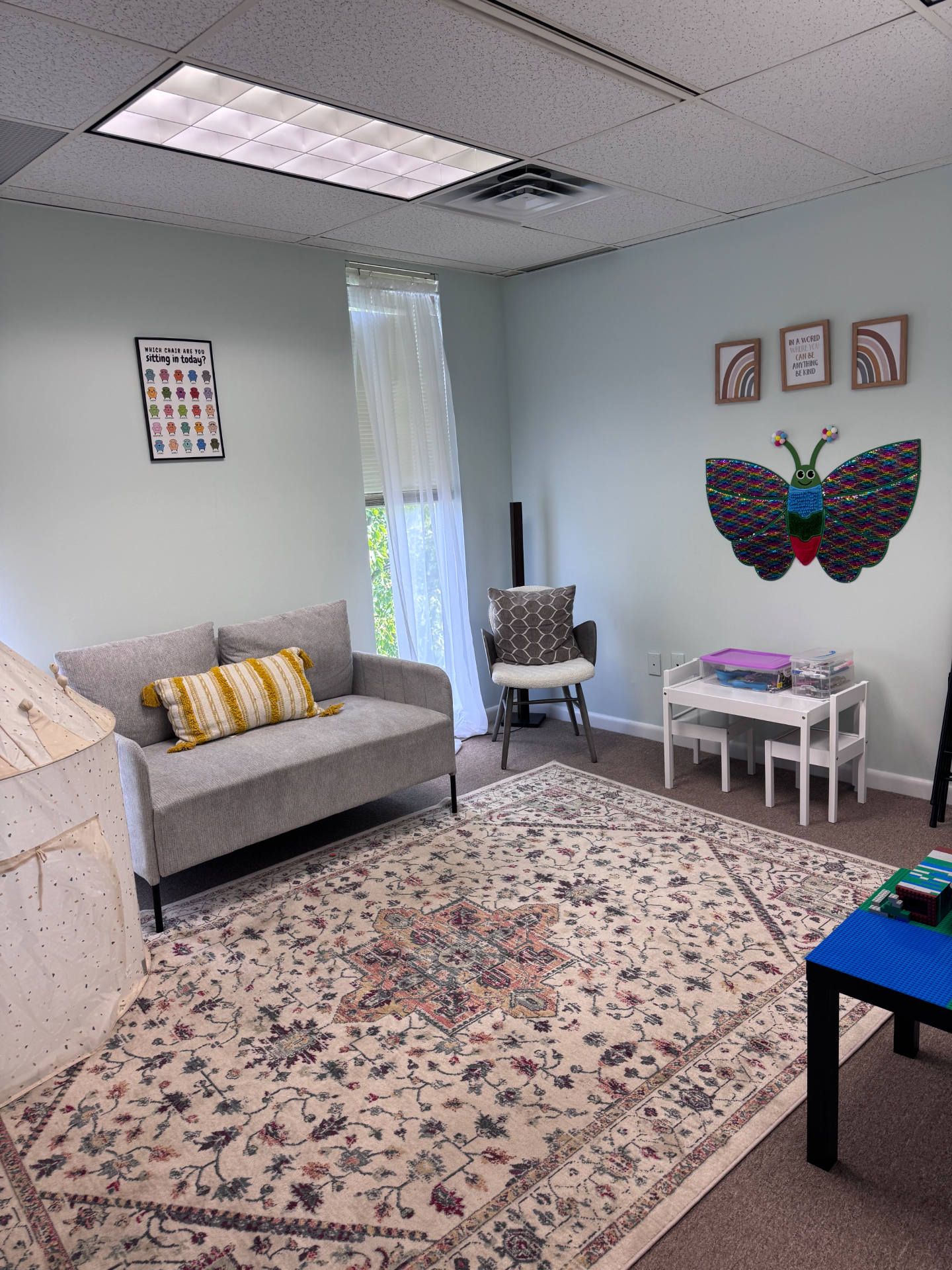 Children's therapy room with a grey loveseat, play tent, and kids' table